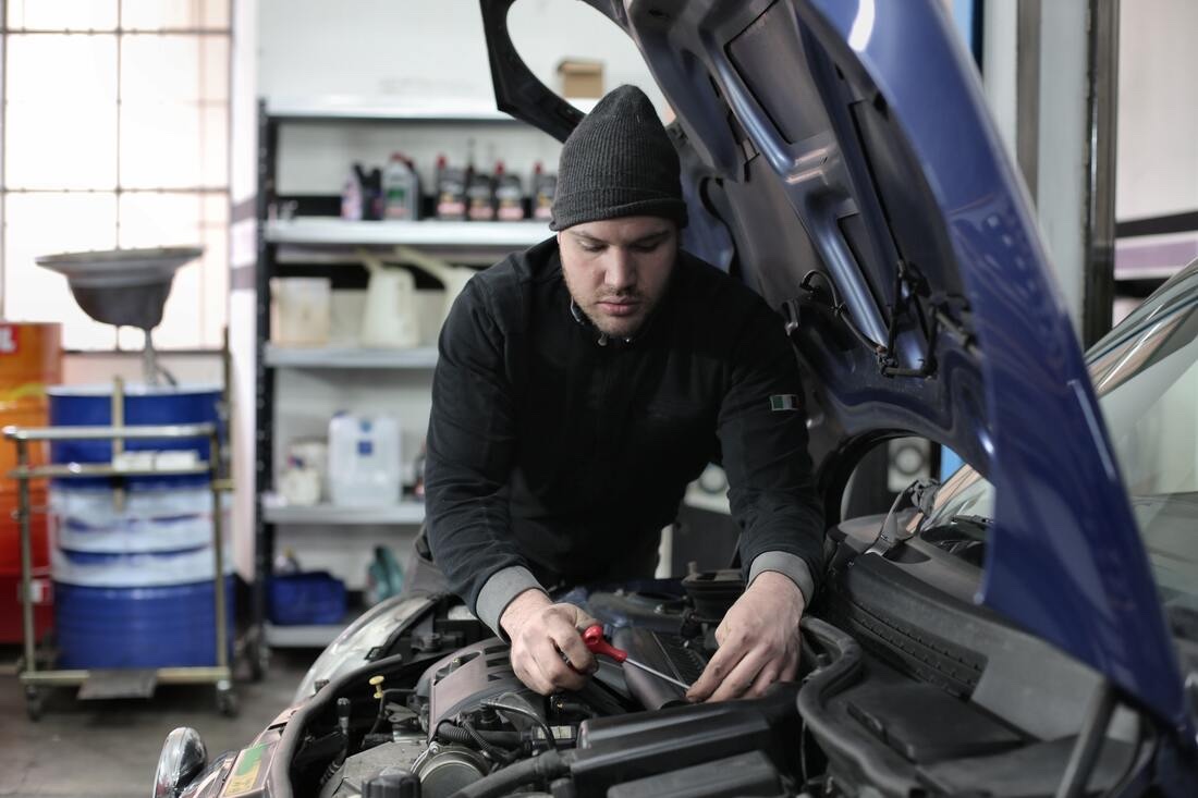 A technician leaning under the hood of a car in the shop.